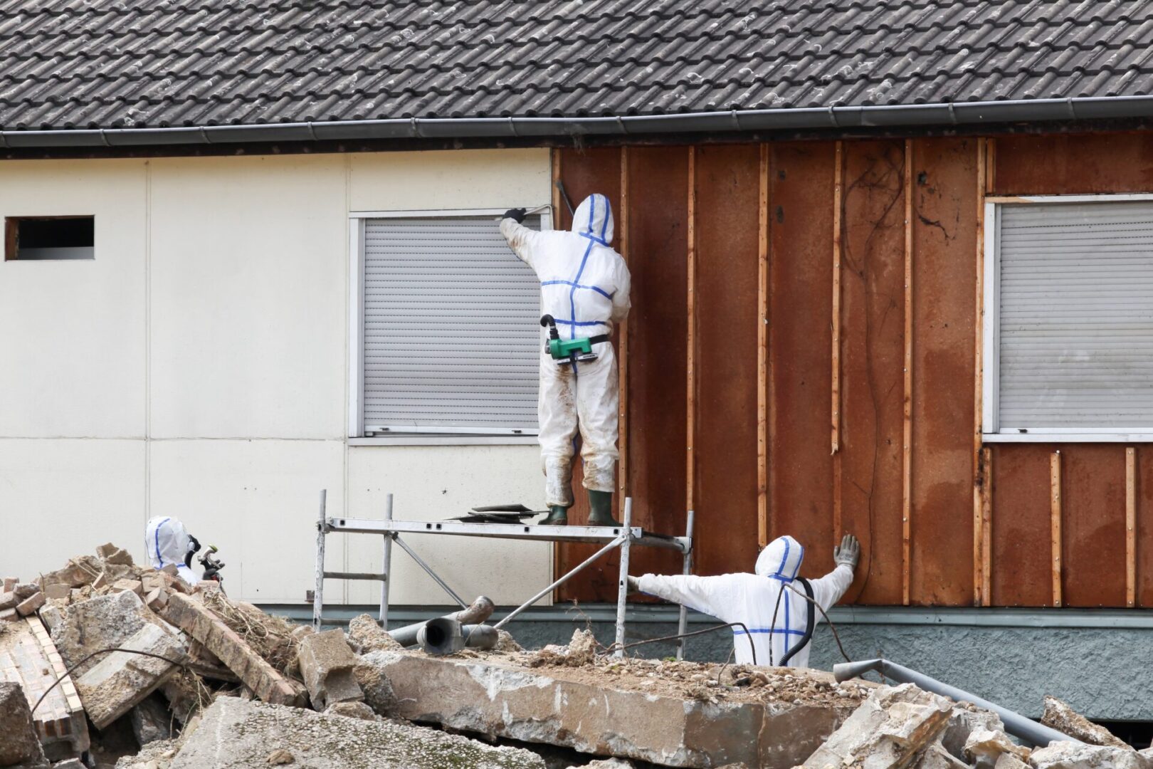Workers in protective suits renovating house exterior.
