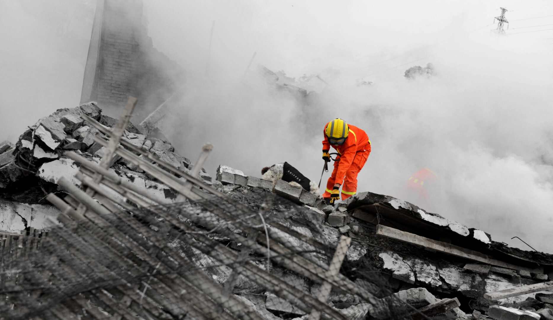 Rescue worker on rubble amidst smoke.