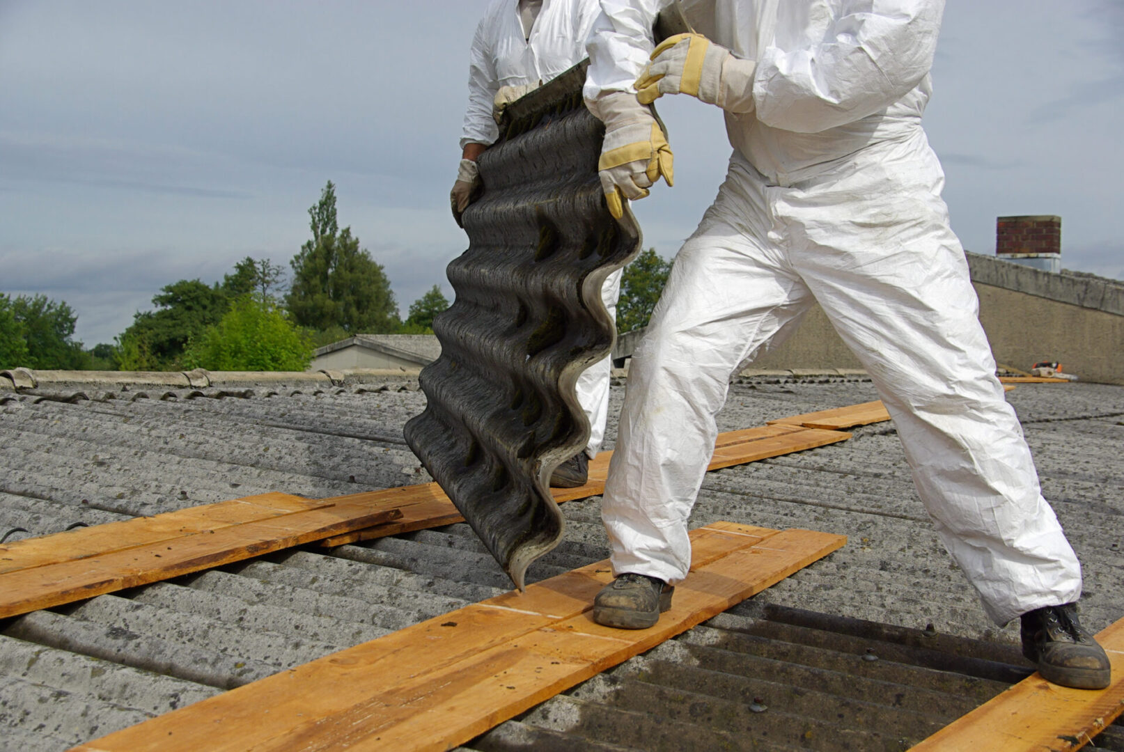 Workers removing asbestos roof in protective suits.